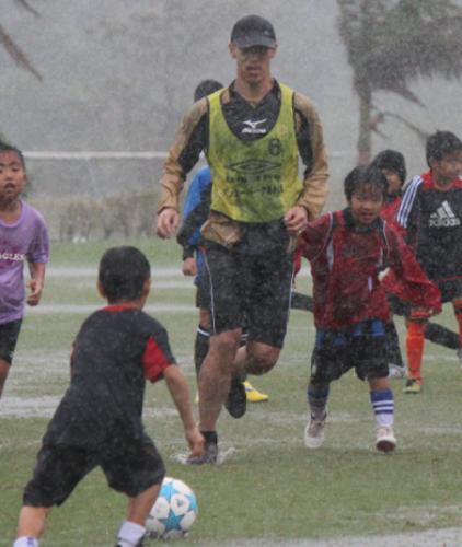 大雨の中、子どもたちにサッカー教室を行う本田