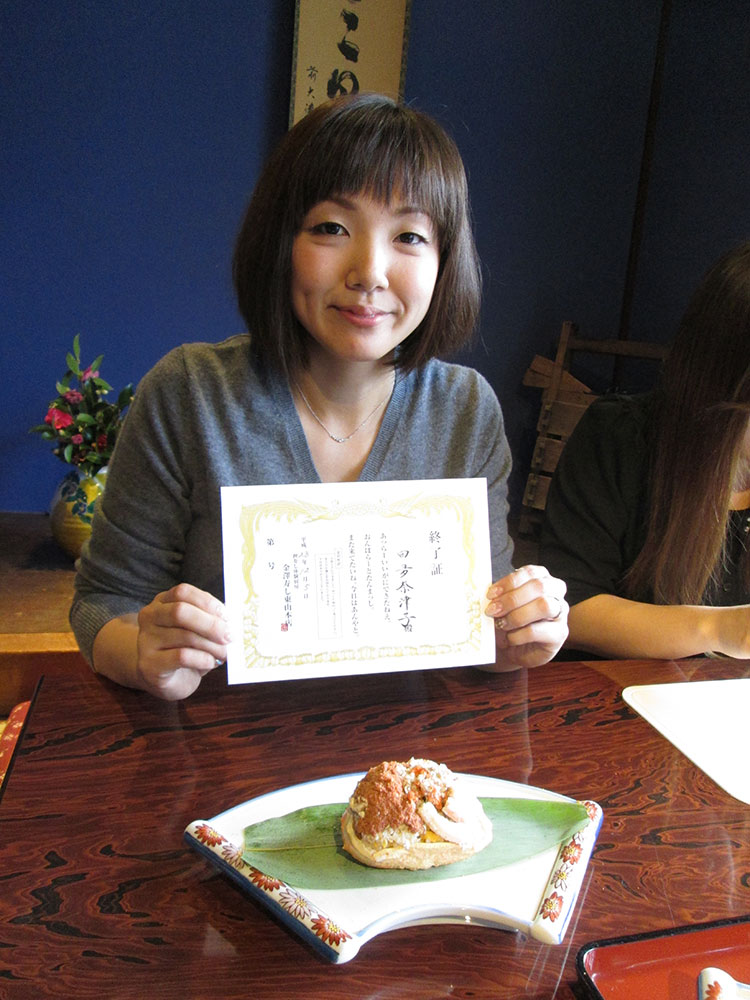 完成した香箱カニ面寿司を前に修了書を手にして喜ぶ女性客