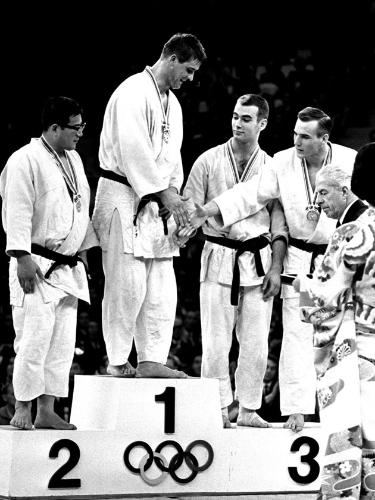 東京五輪柔道の無差別級で金メダルを獲得し、表彰式で握手を求められるヘーシンク。左端は神永昭夫（６４年、日本武道館）