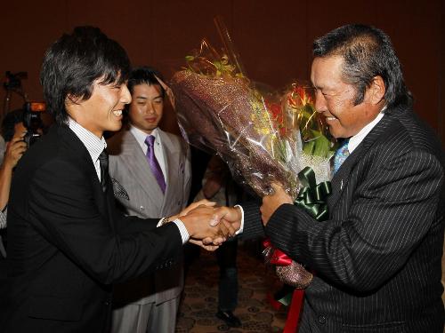 世界ゴルフ殿堂入りが決まった尾崎将司（右）に、池田勇太（中）が見守る中、祝福の花束を渡す石川