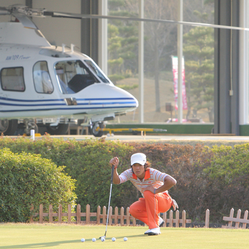 ゴルフ場にとめられたヘリコプターの前でパッティング練習をする石川