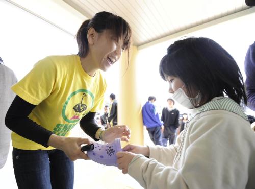 避難所を訪れ、子どもが持ってきたサンダルにサインする高橋尚子さん（左）