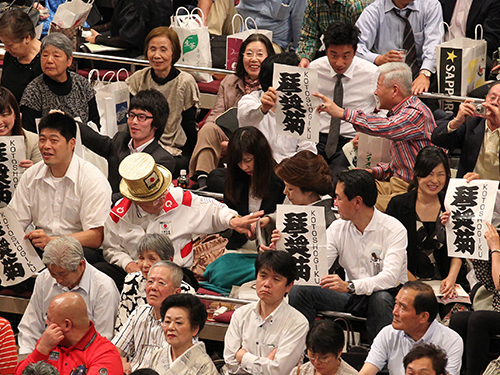 お気に入りの力士のしこ名が入った紙切れを取組前にたまり席で配る山田直稔さん（中央左）