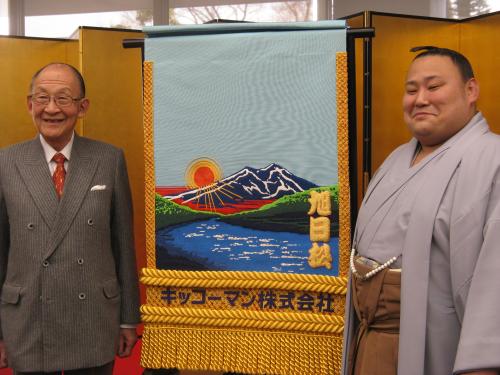 茂木友三郎キッコーマン名誉会長と化粧まわしの前で笑顔の旭日松（右）