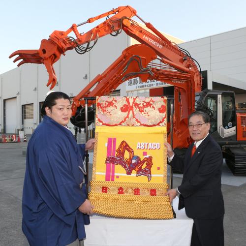 木川理二郎・日立建機会長より「超重機アスタコ」をデザインした化粧回しを贈呈される遠藤（左）