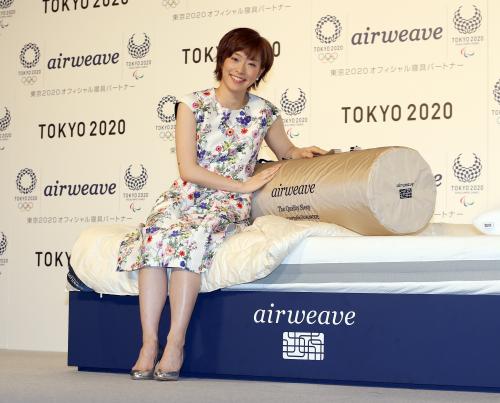２０２０年東京五輪とパラリンピック公式エンブレムを背にベッドに座りフォトセッションを行う石川佳純