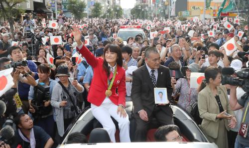 レスリングの伊調馨（手前左）。出身地の青森県八戸市で行われたパレードで観衆に向かい笑顔で手を振った。隣は母の遺影を持つ父春行さん