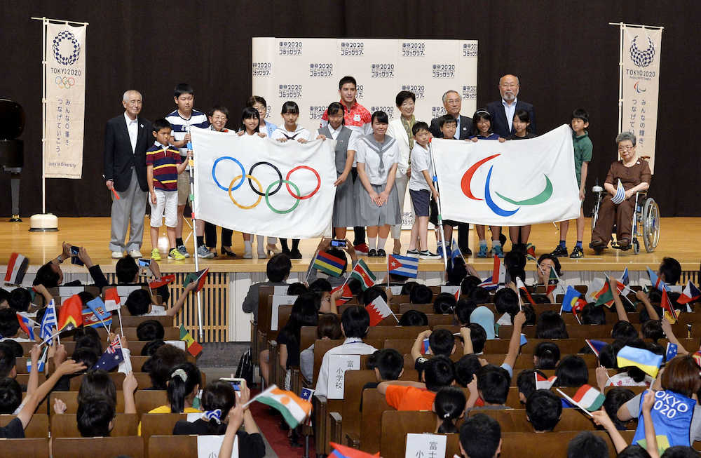五輪旗とパラリンピック旗を披露する「フラッグツアー」のイベントで記念写真に納まる東京都の小池百合子知事（後列右から３人目）、ベイカー茉秋選手（同４人目）ら