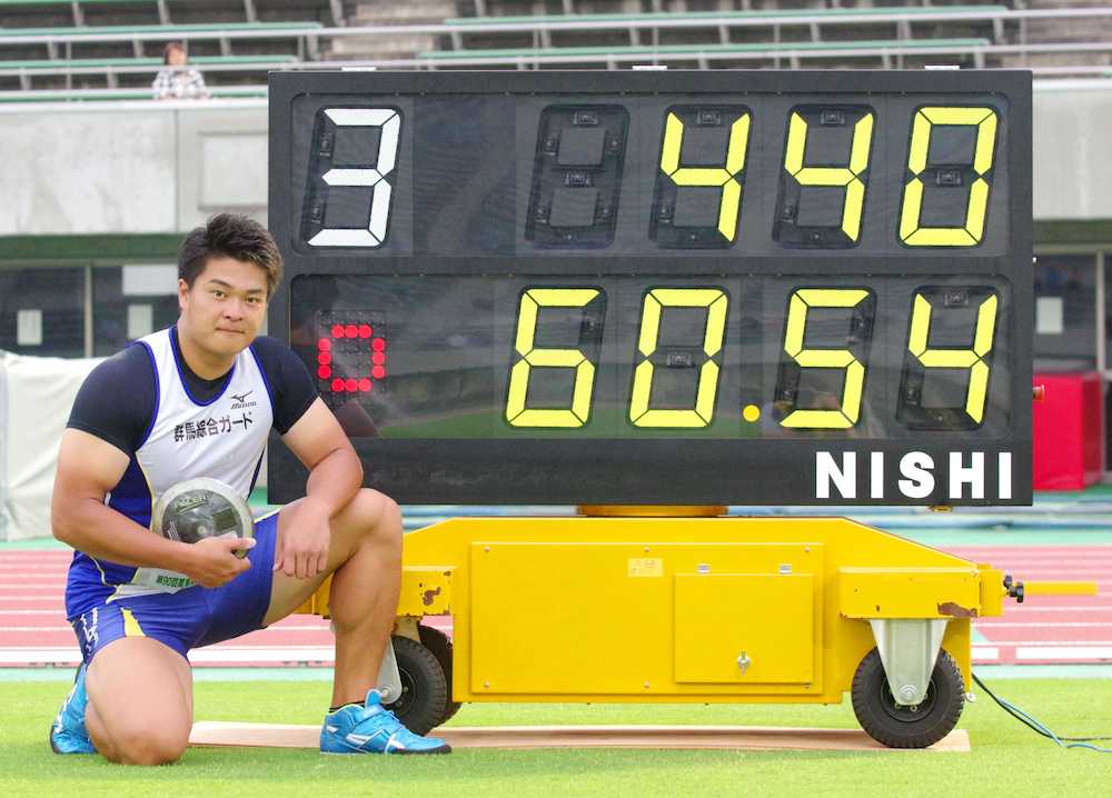 男子円盤投げで６０メートル５４の日本新記録を樹立し、ボードの前でポーズをとる堤雄司