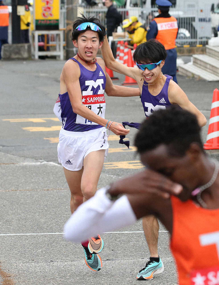 【画像・写真】、3区・手嶋にたすきを繋ぐ明大・加藤（左）（撮影・会津　智海）