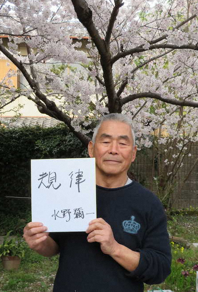自宅の桜の前で「規律」のメッセージを掲げる水野弥一氏