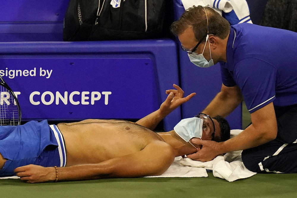 試合中、トレーナーから首の治療を受けるジョコビッチ(AP)