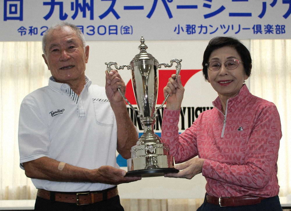 九州スーパーシニアカップゴルフで、2年ぶり2度目の優勝を決めた藤本隆（左）と女子の部初代女王の福井和子はカップを手に笑顔