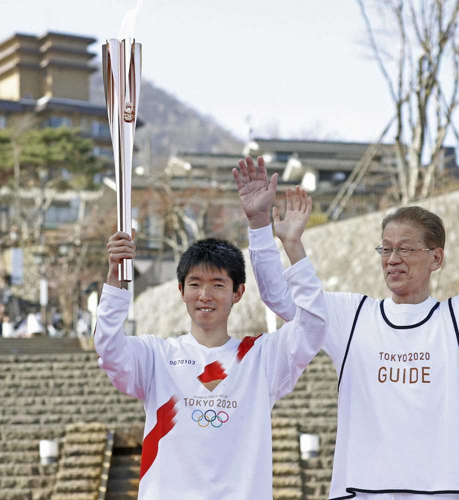 聖火を掲げて笑顔を見せる、東京パラリンピック代表に内定している陸上の唐沢剣也選手（左）