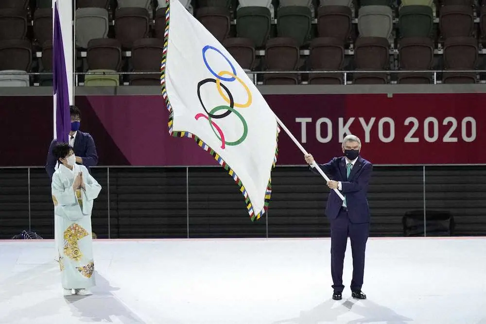 【画像・写真】東京都の小池百合子知事（左）から受け取った五輪旗を振るIOCのバッハ会長（共同）